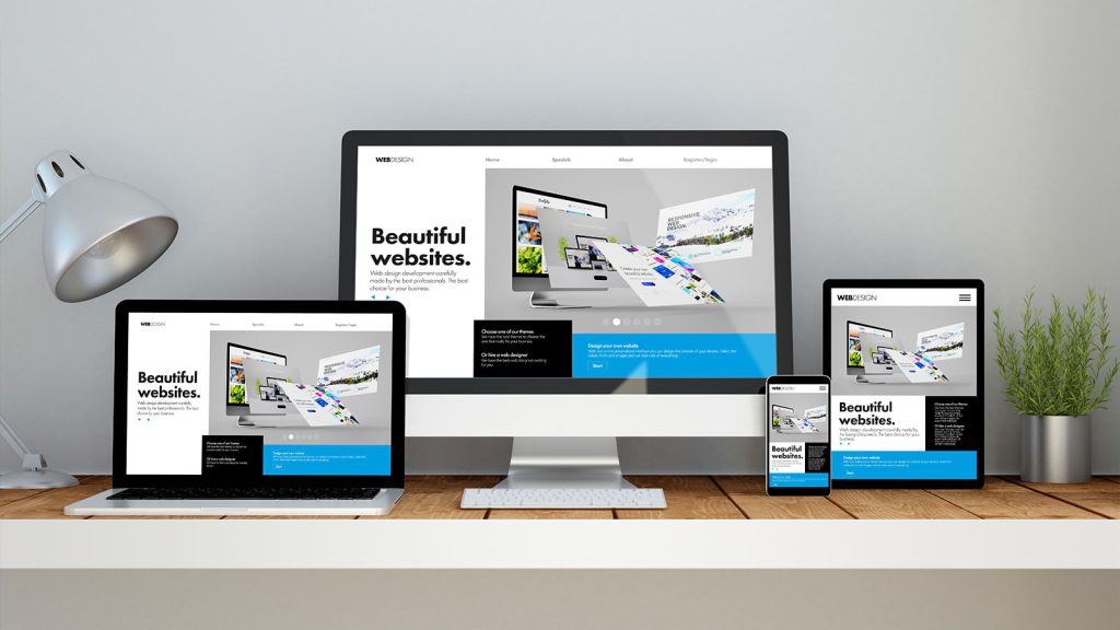 Ffour different sized screens sitting on a shelf, each with the same web page on display. There's an Imac, a Macbook, a Tablet and a Mobile. The backdrop is grey, and either side of the screens are an office lamp to the left, and a potted succulent plant to the right in a silver pot. 